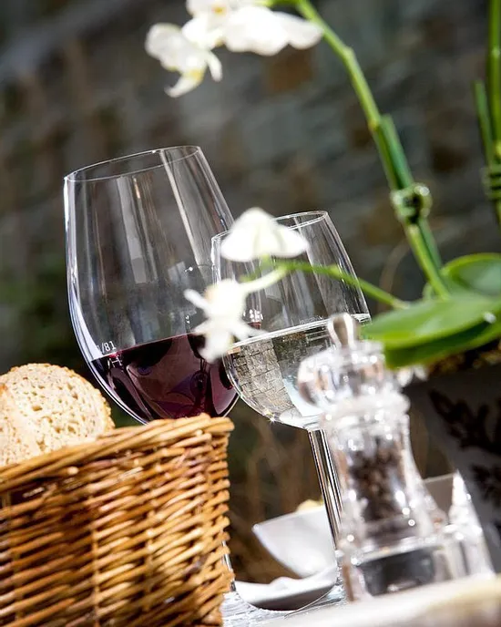 Bicchieri di vino rosso e bianco su tavolo da ristorante con cestino del pane e orchidee bianche